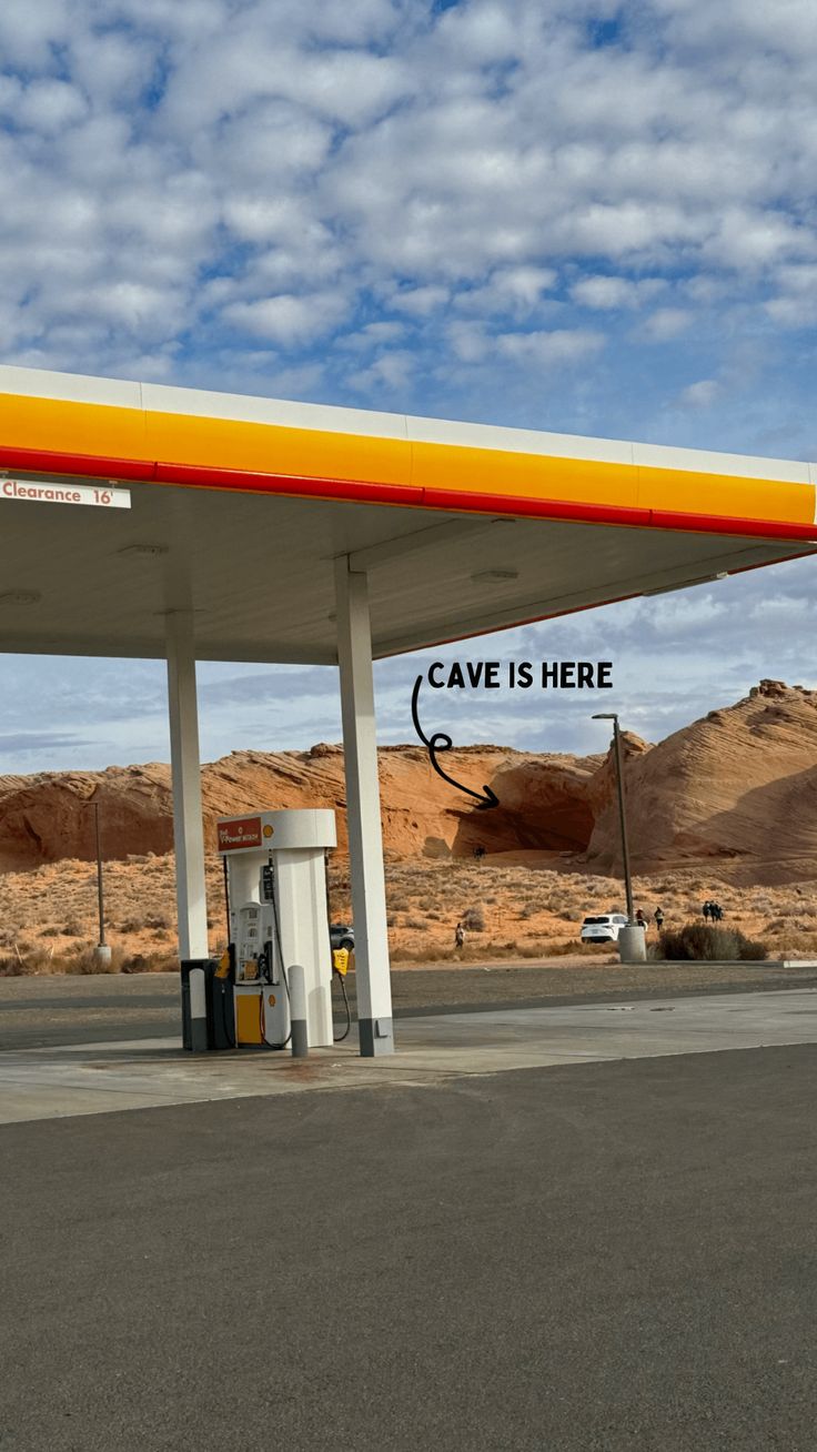 a yellow and red gas station sitting on the side of a road with mountains in the background