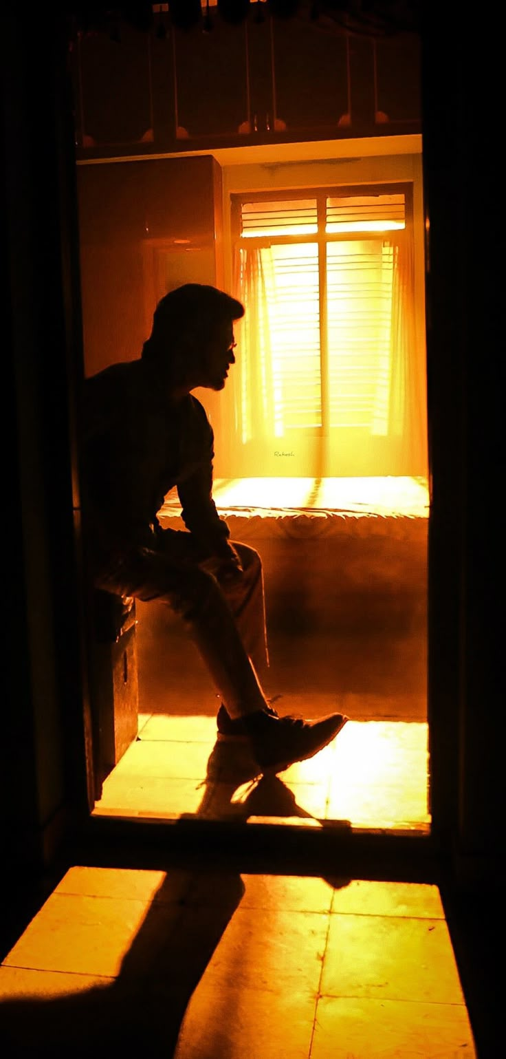 a person sitting on a bench in a dark room with sunlight coming through the window