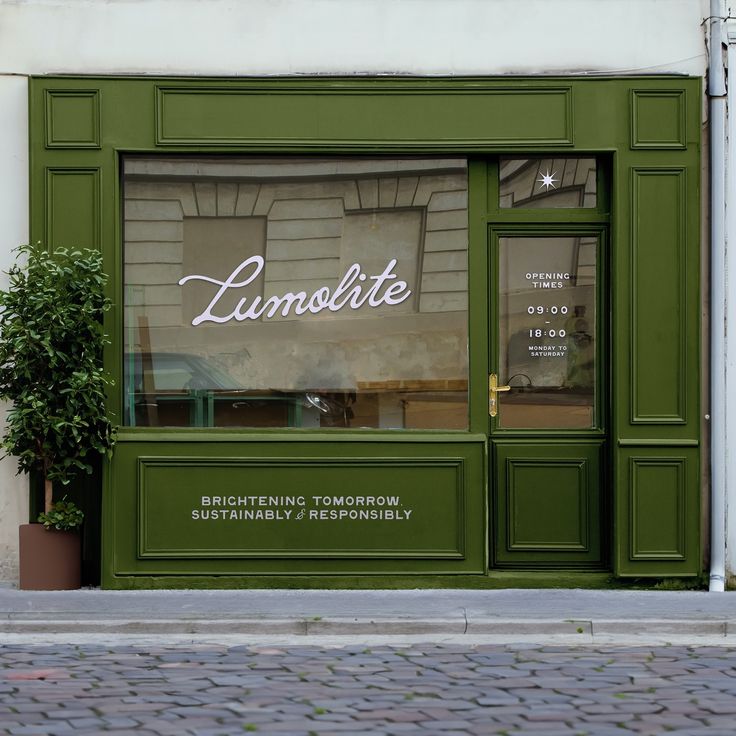 a green storefront on the side of a building with a potted plant next to it