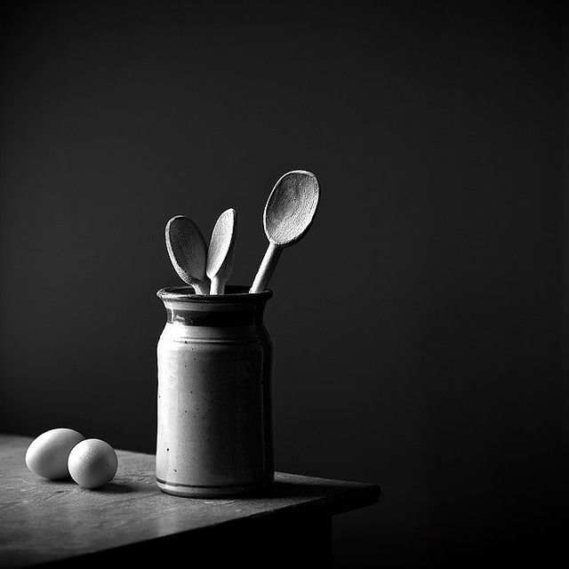 three spoons and two eggs in a jar on a table with a black background