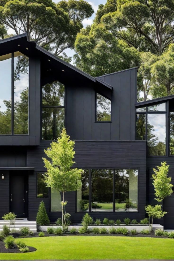 Modern black house with large windows, surrounded by lush greenery and trees. Dark House Landscaping, Charcoal Home Exterior, Black Mid Century House, House Design Dark, Home Exterior Black, Black Contemporary House, All Black Houses, Black Exterior House, All Black House Exterior