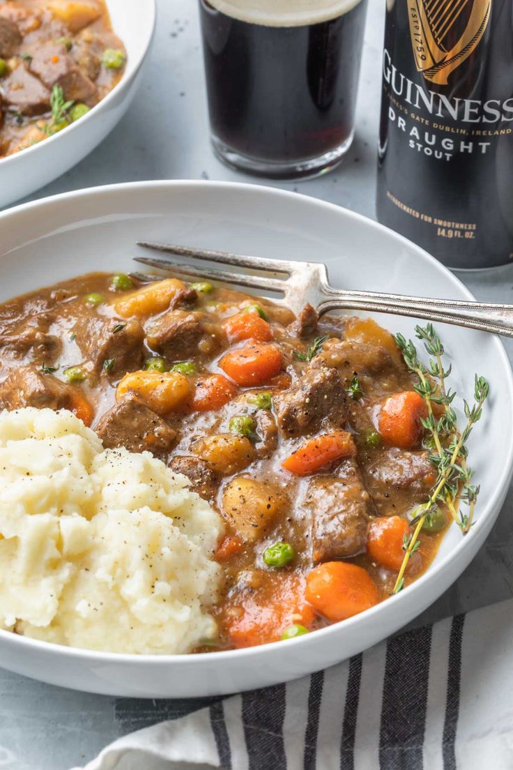 a bowl filled with meat, potatoes and carrots next to a bottle of guinness