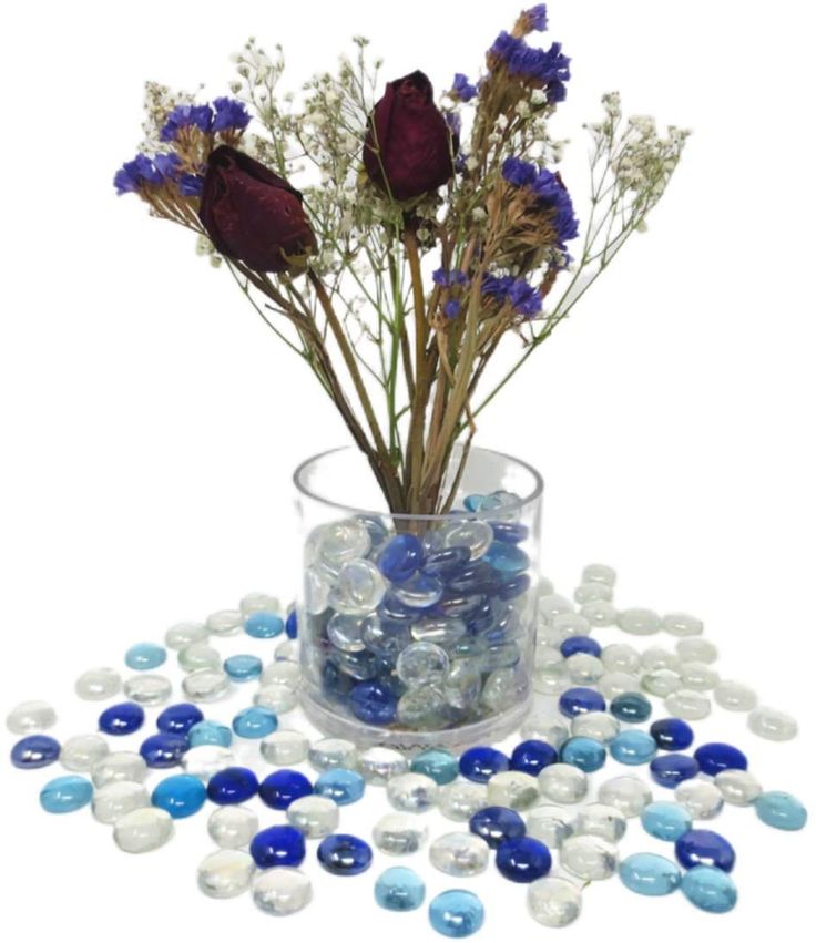 a vase filled with lots of blue and white marbles next to some flowers in it