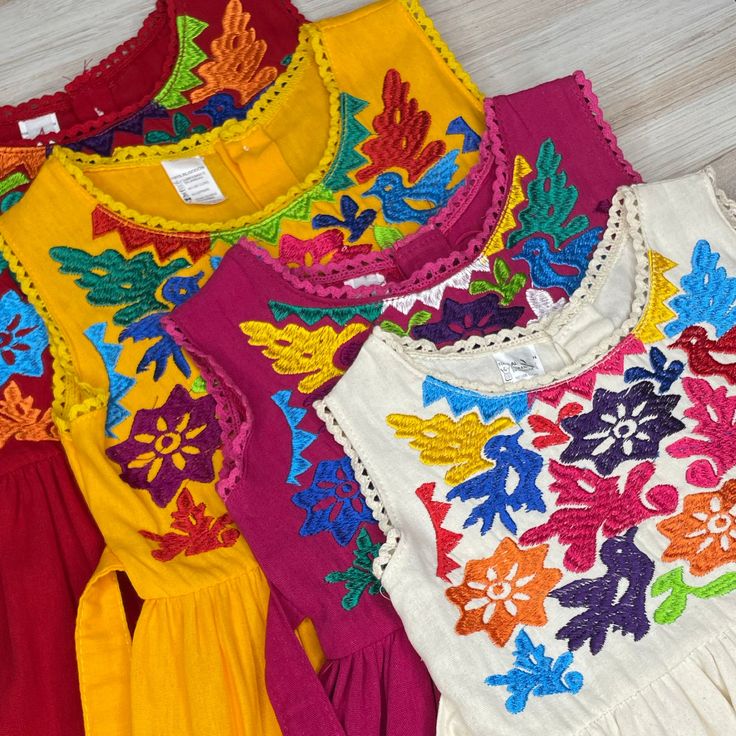 three different colored blouses are sitting on the floor next to each other and one has an embroidered flower design