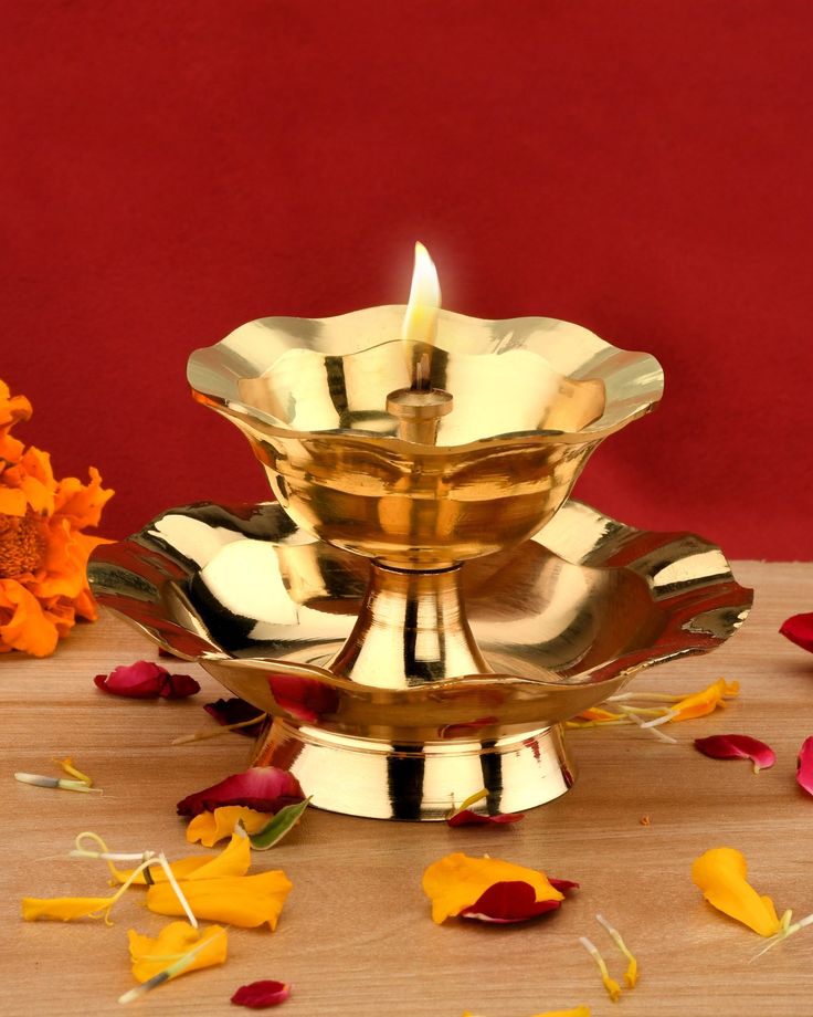 a golden candle is sitting on top of a gold plate with petals around it and red wall in the background