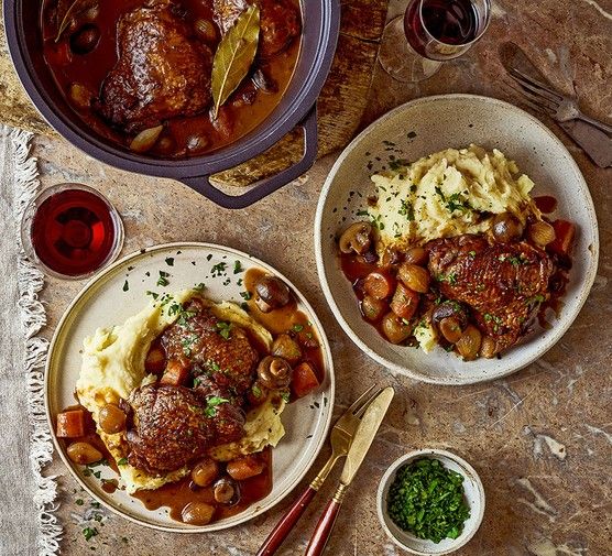 two plates with meatballs, mashed potatoes and gravy next to wine glasses