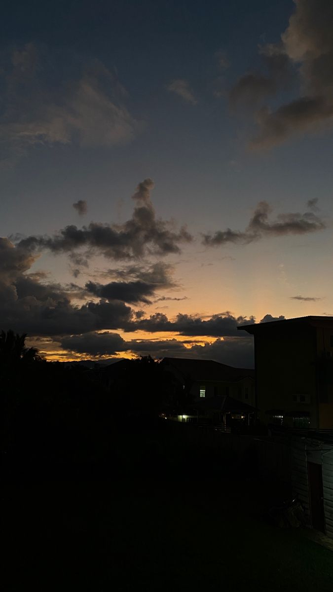 the sun is setting behind some clouds in the sky over a building and grass area