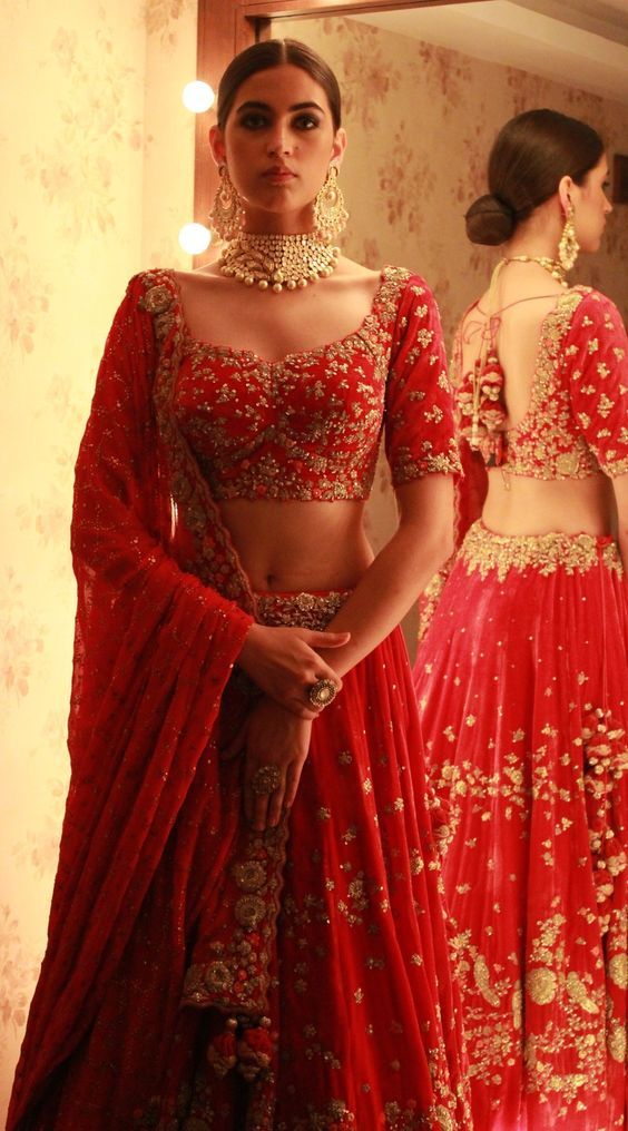 a woman in a red lehenga and matching blouse with gold embellishments