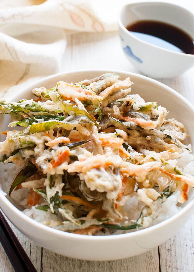 a white bowl filled with rice and veggies next to chopsticks on a table