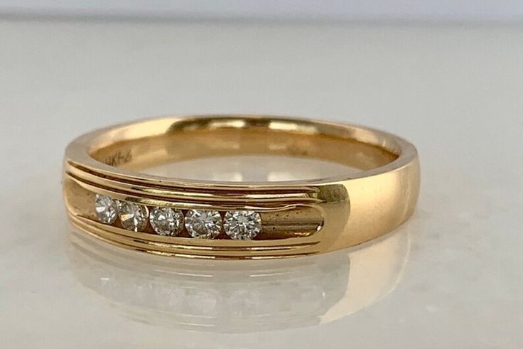 a yellow gold wedding ring with three diamonds on the side, sitting on a white surface