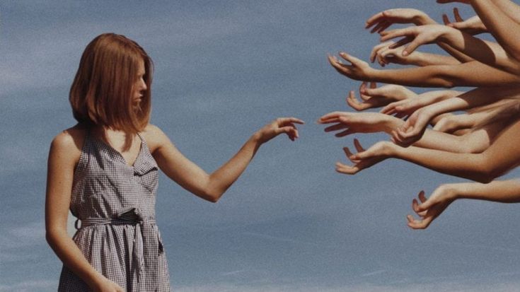 a woman standing in front of a group of hands reaching out to touch her hand