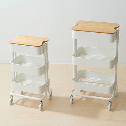 two white serving trolleys with wooden top and bottom trays on wheels, against a white wall