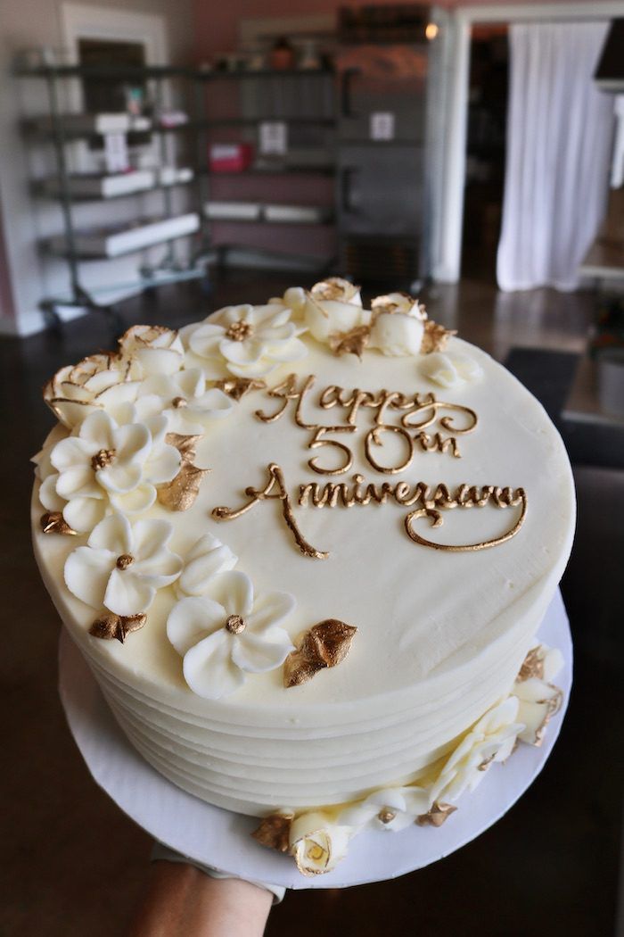 a birthday cake with white frosting and gold lettering on the top that says happy 50th anniversary