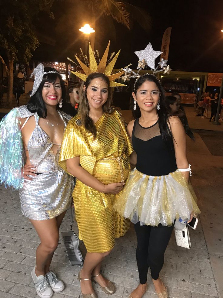 three women dressed up in costumes posing for the camera at an outdoor event with palm trees behind them