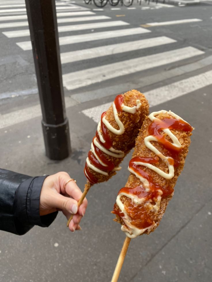 someone is holding two skewers with meat and sauce on them in the street