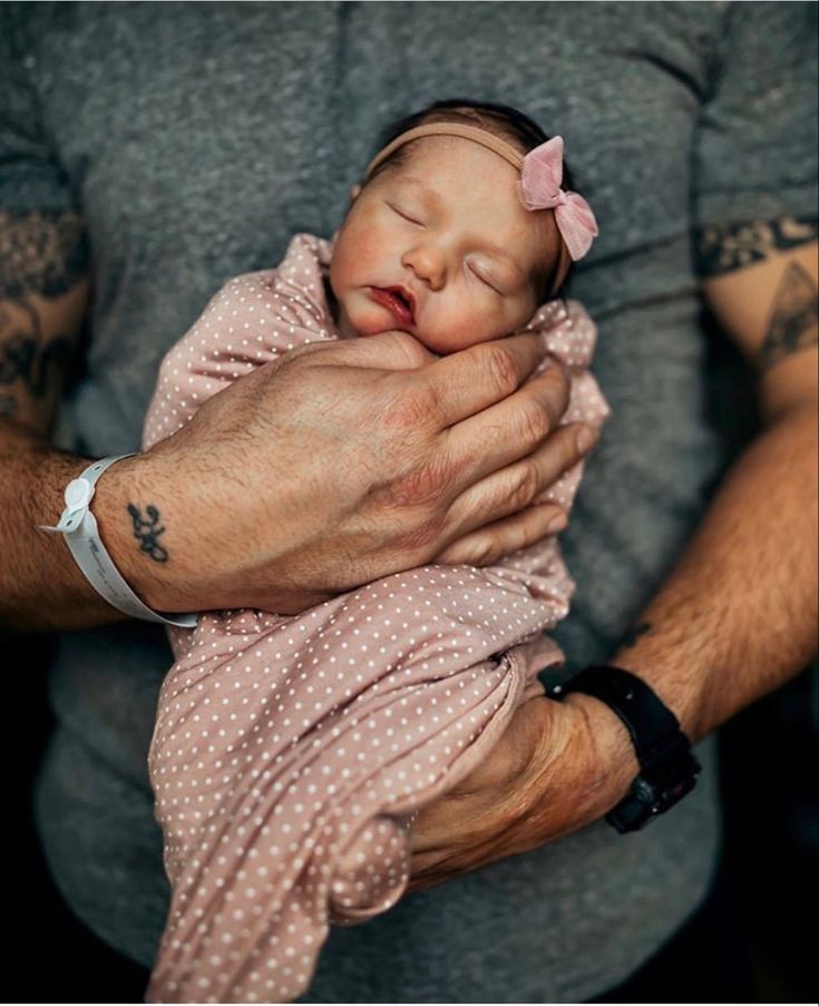 a man holding a newborn baby in his arms and wearing a pink bow on it's head