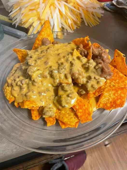 nachos with cheese sauce and tortilla chips on a clear glass plate