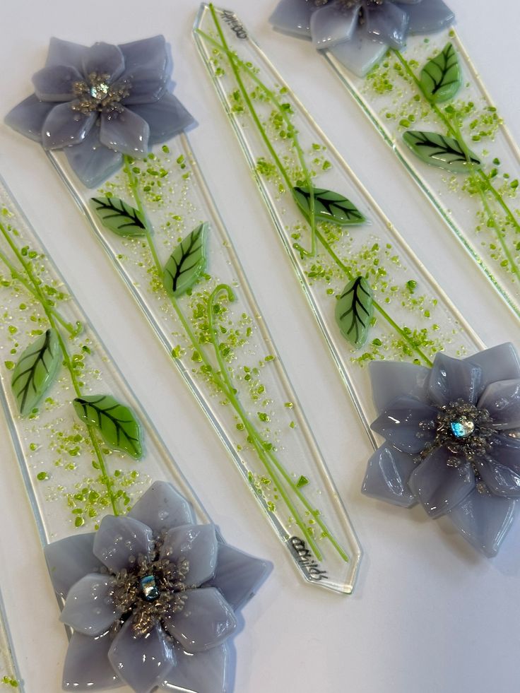 four flower shaped hair pins with green leaves and flowers on them, sitting next to each other