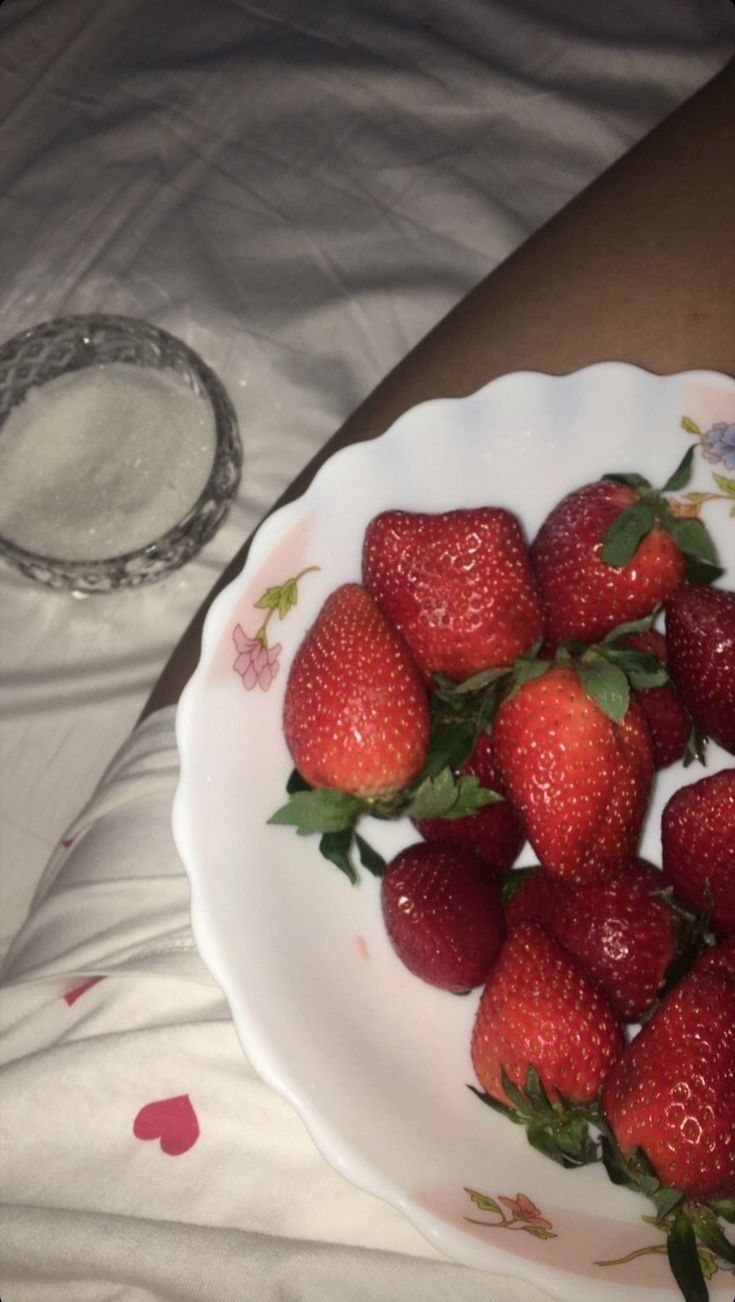 a white plate topped with strawberries on top of a bed next to a person's arm