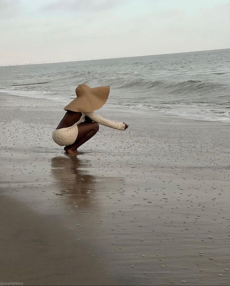 a woman kneeling on top of a beach next to the ocean