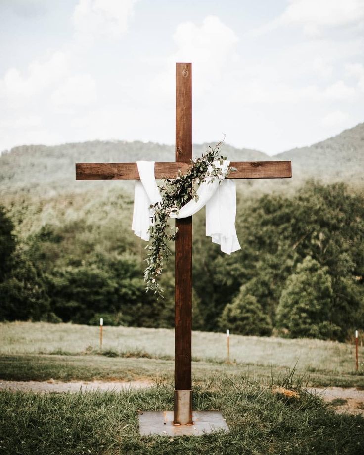 a cross decorated with flowers and greenery in front of a mountain backdrop for an outdoor wedding