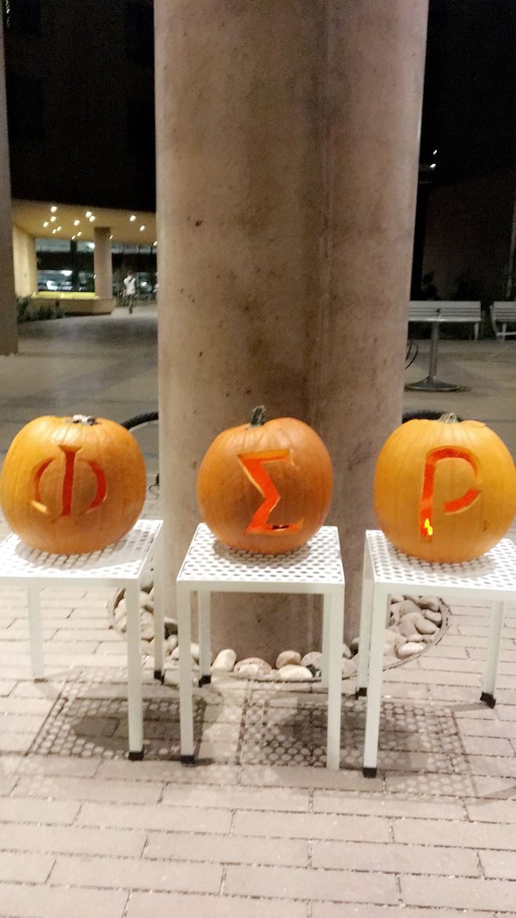 three pumpkins with the letter d carved into them sitting on small white tables in front of a pillar