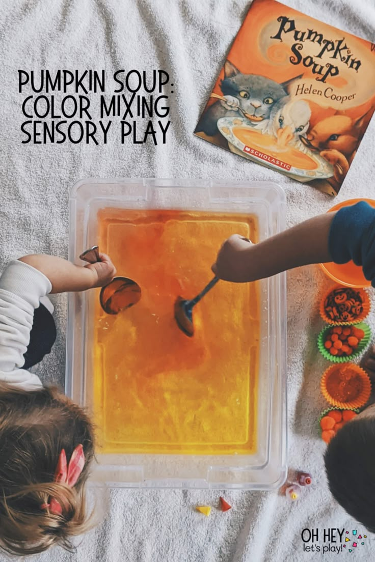 two children are playing with pumpkin soup in an orange plastic container on a white blanket