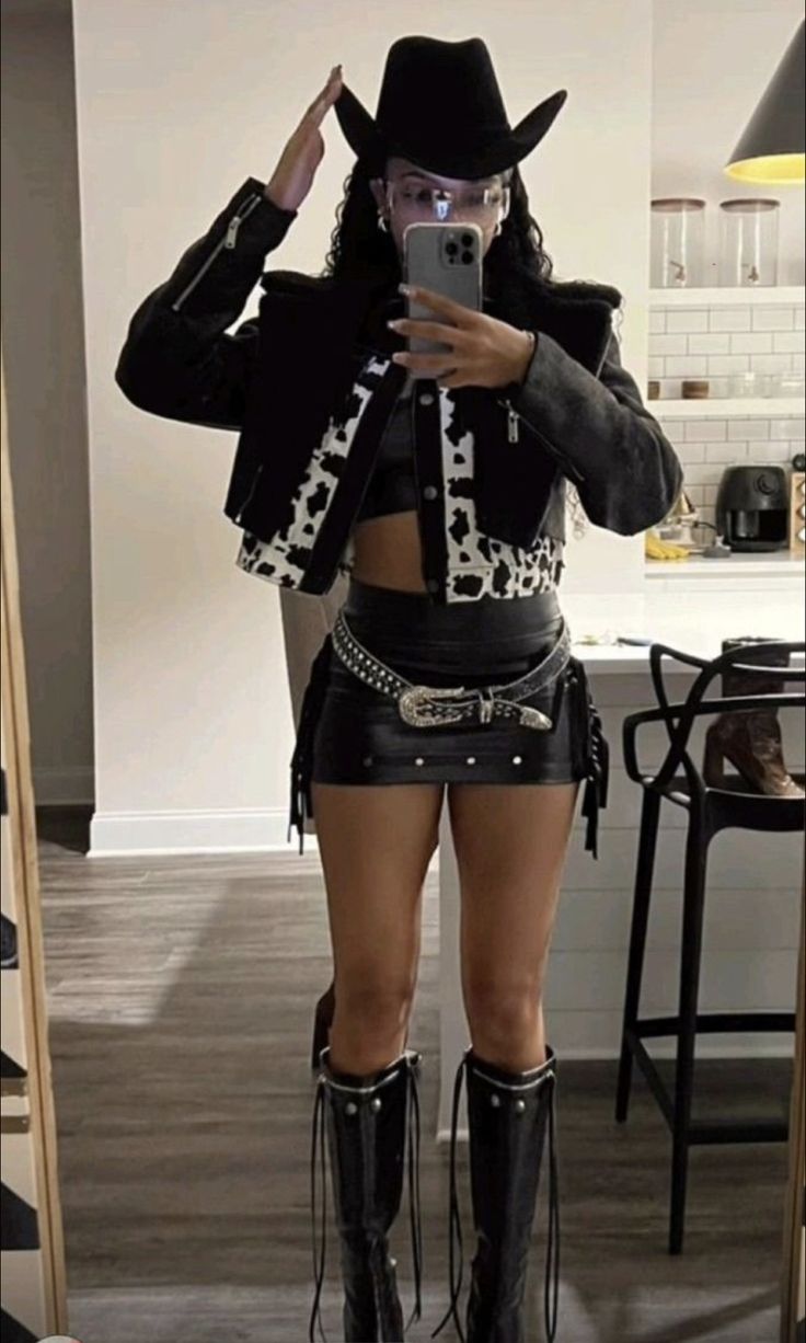 a woman in black boots and cowboy hat taking a selfie with her cell phone