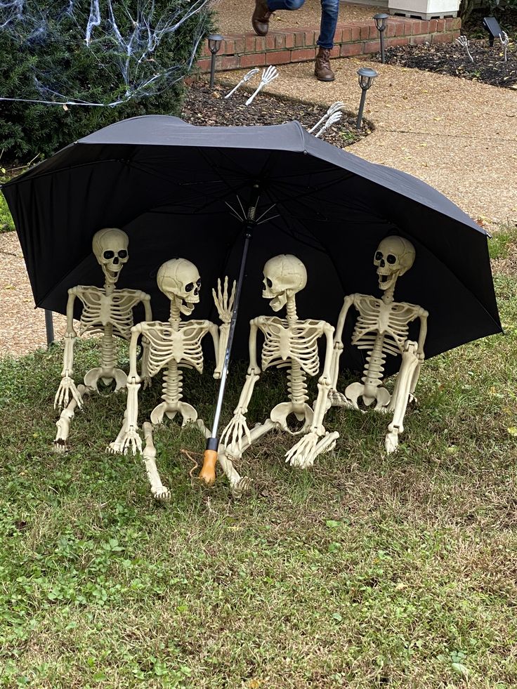 three skeletons sitting under an umbrella in the grass