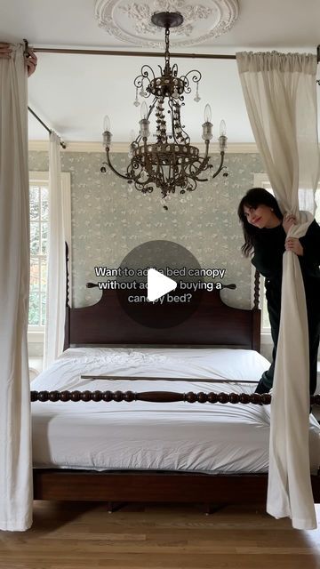 a woman opening curtains in front of a bed with a chandelier hanging from the ceiling