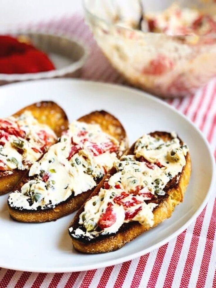 some bread with cheese and other toppings on a white plate next to a red and white checkered table cloth