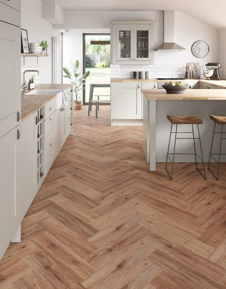 a kitchen with wooden flooring and white cabinets is pictured in this image, there are two stools on the counter