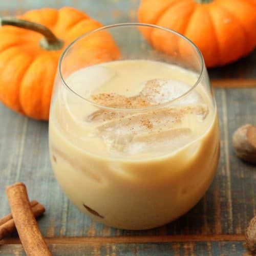 there is a drink in a glass with cinnamon on the table next to pumpkins