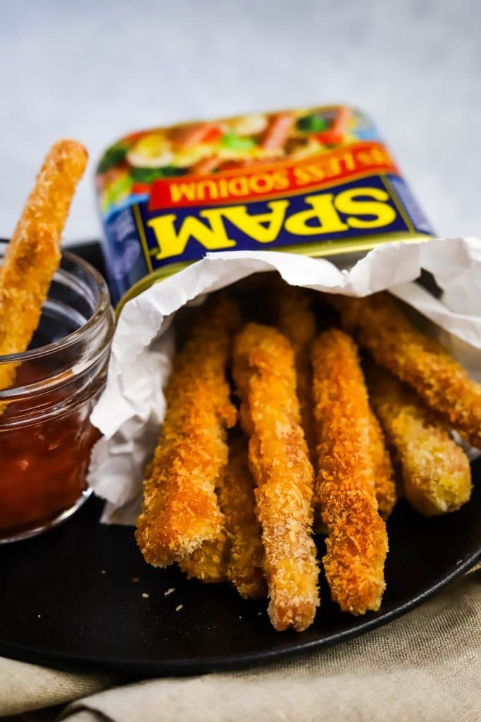 some fried food on a black plate with a jar of ketchup