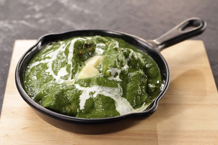 a pan filled with spinach and cheese on top of a wooden cutting board