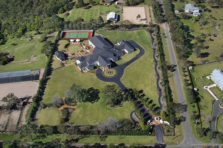 an aerial view of a large house surrounded by green grass and lots of trees in the background