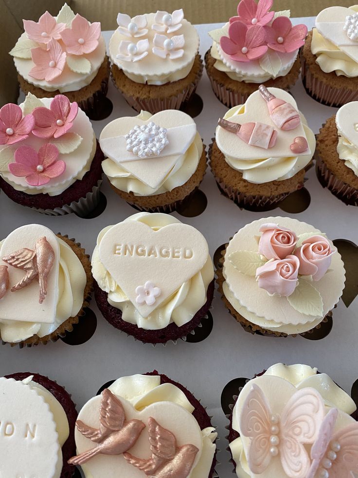 a box filled with lots of cupcakes covered in white frosting and pink icing