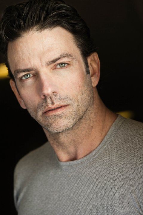 a close up of a person wearing a gray shirt and looking at the camera with a serious look on his face