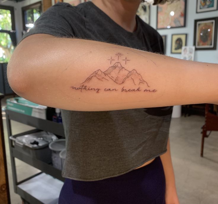 a woman with a tattoo on her arm that says nothing can break me in the mountains