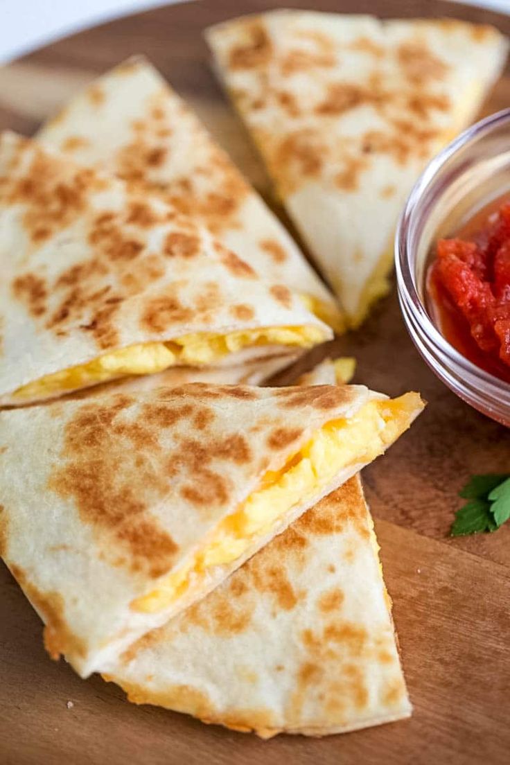 several quesadillas on a wooden plate with salsa in a small glass bowl