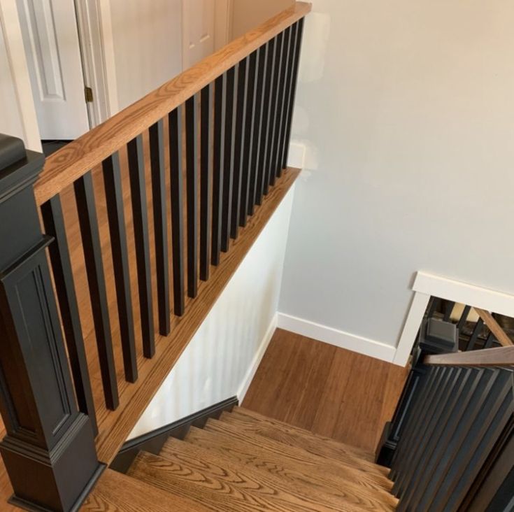 a wooden stair case next to a white door and black railing on top of a hard wood floor