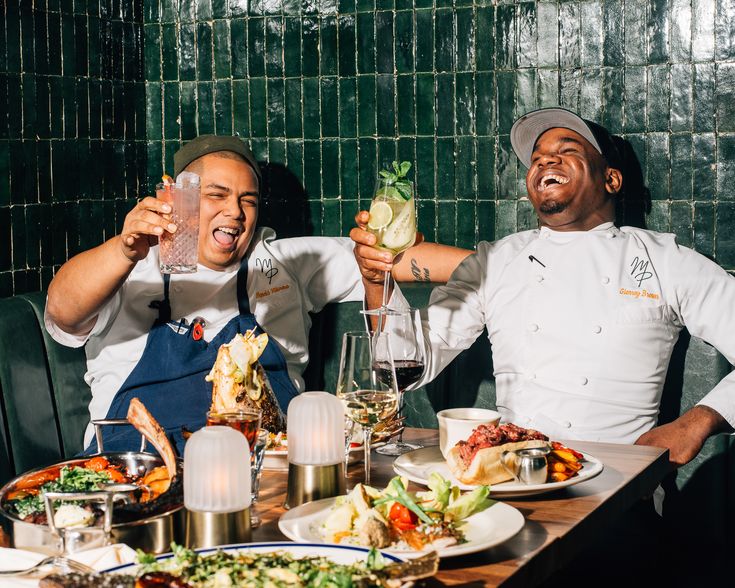 two men sitting at a table with food and drinks