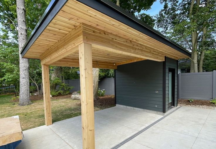 an outdoor covered patio area with a bench and storage shed in the back ground, surrounded by trees