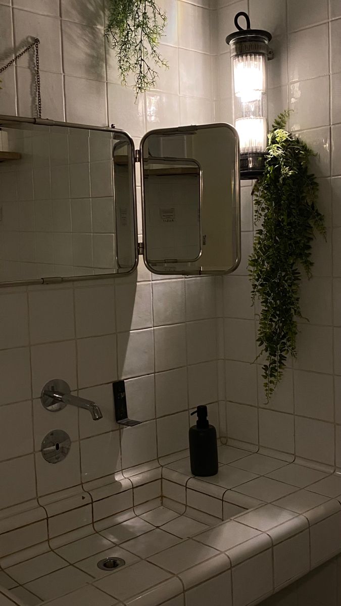 a bathroom with white tiles and plants hanging on the wall next to it's mirror