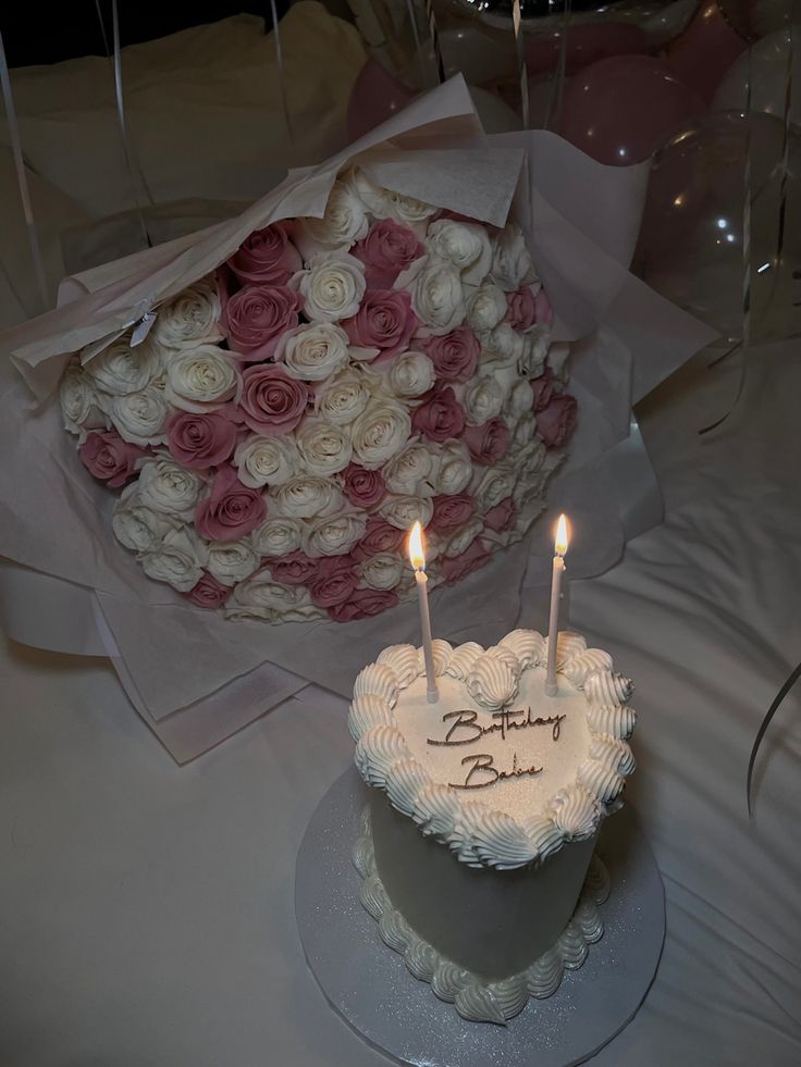 a heart shaped cake with two candles on it sitting on a table next to a bouquet of roses