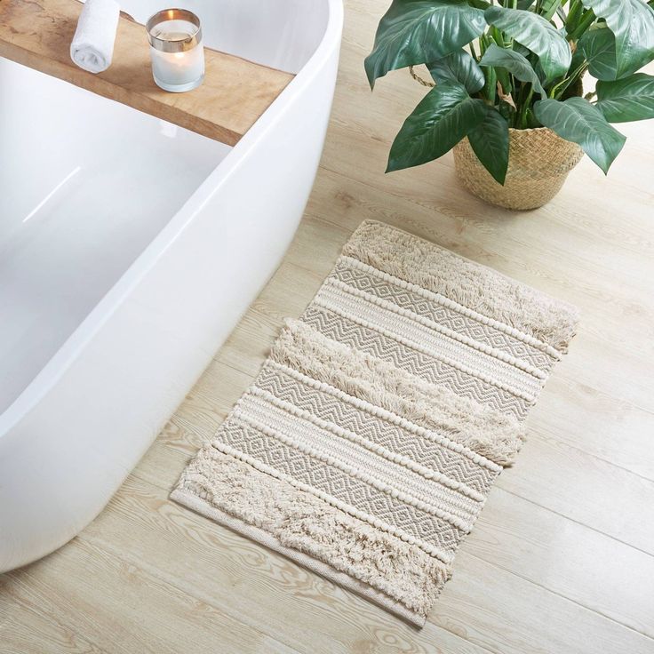 a bath tub sitting next to a plant and a rug on top of a wooden floor