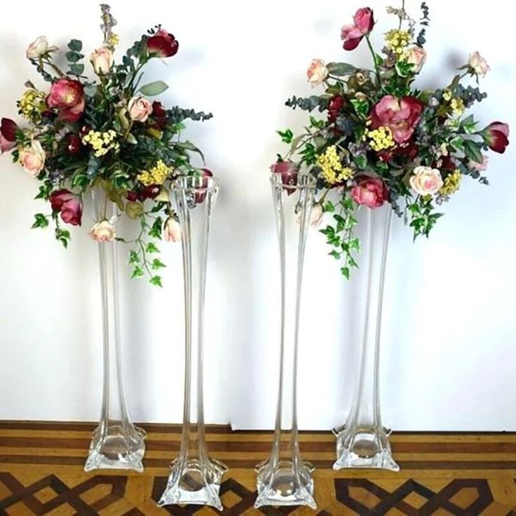 two tall vases with flowers in them sitting on a floor next to each other