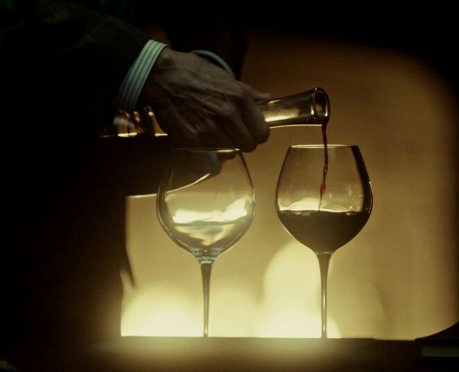 a person pouring wine into two glasses on a table with the light from behind them