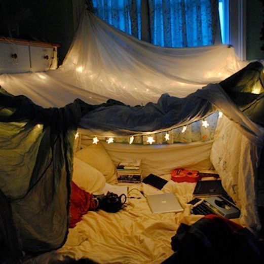 an unmade bed in a room with lights on the ceiling and curtains over it