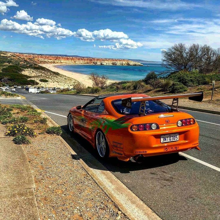 an orange sports car is parked on the side of the road by the beach and ocean